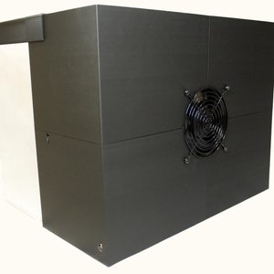 May include: A dark gray soundproof booth with a metal fan on the side. The booth has a white door.