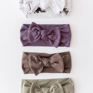 May include: Four different fabric headbands with knotted bows. The headbands are in a variety of colours, including grey, purple, brown, and green.