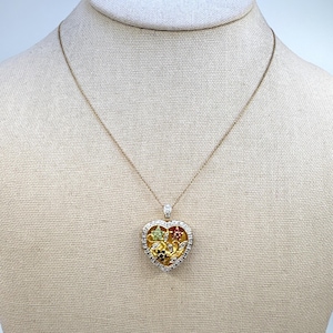 May include: A gold-toned heart pendant necklace. The heart-shaped pendant features a gold interior with colorful gemstones and is outlined with clear stones. The necklace is displayed on a neutral-colored surface.