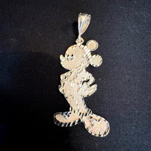May include: A silver-toned metal pendant shaped like a cartoon mouse character. The surface features a combination of textured, matte, and polished finishes with diagonal striped detailing throughout the body and ears, including a top bail loop.