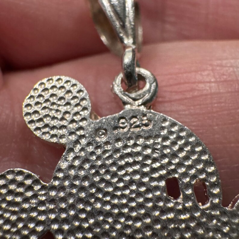 May include: A silver-coloured metal pendant shaped like a mouse head with a textured, dimpled surface. The back of the pendant features a copyright symbol and the stamp 925, indicating sterling silver composition, with a small metal loop at the top.