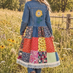 May include: A long denim jacket featuring a sunflower embroidery on the upper back and a multi-patterned patchwork skirt section. The lower hem is finished with a wide white lace trim. The jacket has long sleeves and a button-up front closure.