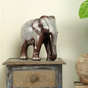 Puede incluir: Una figura de elefante de madera marr&oacute;n oscuro con patrones florales y de puntos blancos. El elefante est&aacute; sobre una peque&ntilde;a mesa ornamentada. El logotipo de Craft by Soul es visible en la esquina superior derecha.