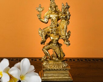 May include: A gold-coloured statue depicting multiple figures in a layered arrangement. The statue is on a square base and features intricate details. The background is a solid orange colour. White flowers are in the foreground.