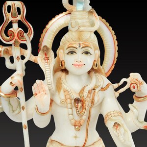 May include: A white and beige statue of a seated deity with multiple arms, adorned with jewelry and a serpent. The statue holds a trident and a small vessel. The base features a lion's head. The statue has gold accents and is set against a black background.