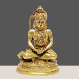K&ouml;nnte beinhalten: Eine goldene Messingstatue von Hanuman, einer hinduistischen Gottheit, in einer sitzenden Meditationshaltung. Die Statue weist komplizierte Details auf, darunter aufwendiger Schmuck und eine Krone. Die Figur sitzt auf einem detaillierten Sockel, mit einer Keule daneben.