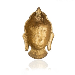 Puede incluir: Un colgante de cabeza de Buda dorado con una superficie texturizada. El colgante tiene una parte superior puntiaguda y rasgos faciales detallados, incluida una expresi&oacute;n serena. El colgante probablemente est&aacute; hecho de metal y est&aacute; dise&ntilde;ado para joyer&iacute;a o fines decorativos.