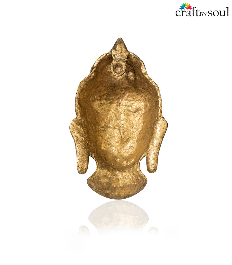 Puede incluir: Un colgante de cabeza de Buda dorado con una superficie texturizada. El colgante tiene una parte superior puntiaguda y rasgos faciales detallados, incluida una expresi&oacute;n serena. El colgante probablemente est&aacute; hecho de metal y est&aacute; dise&ntilde;ado para joyer&iacute;a o fines decorativos.