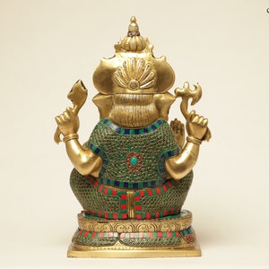 May include: A gold-colored statue of the Hindu deity Ganesha, viewed from the back. The statue features a green, red, and blue mosaic pattern on the back and belly. The deity holds a weapon in one hand and a sweet treat in the other.