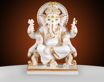 May include: A white marble statue of the Hindu deity Ganesha, seated on a decorative throne. The statue features gold accents on the crown, jewelry, and throne. Ganesha holds a lotus flower and a weapon. The background is a gradient of brown and white.