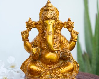 May include: A golden-colored statue of the Hindu deity Ganesha, seated in a meditative pose. The statue has intricate details, including a large head, elephant ears, and multiple arms. The base is round and decorated. The logo "craft by soul" is in the top right corner.