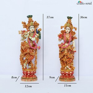 May include: Two ornate statues of Hindu deities. The statue on the left is 37 cm tall, 12 cm wide, and 8 cm deep. The statue on the right is 36 cm tall, 11 cm wide, and 9 cm deep. Both statues feature detailed gold, red, and cream-colored clothing and accessories.