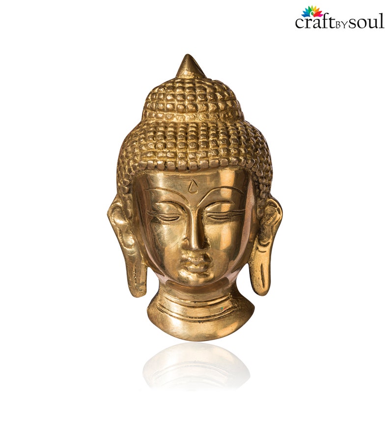 Puede incluir: Una estatua dorada de la cabeza de Buda con los ojos cerrados y una expresi&oacute;n serena. La estatua tiene detalles, incluyendo un tocado texturizado y l&oacute;bulos de las orejas alargados. La base es redonda y la estatua es de lat&oacute;n.