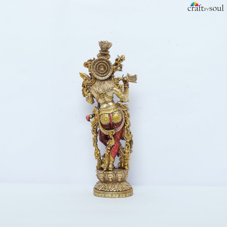 May include: A detailed brass statue of a deity, viewed from the back. The figure is adorned with intricate gold and red detailing, holding a flute. The statue is mounted on a decorative base, showcasing ornate craftsmanship. The logo "craft by soul" is visible in the top right corner.