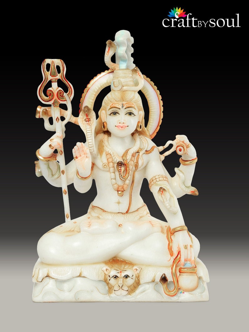 May include: A white and beige statue of a seated deity with multiple arms, adorned with jewelry and a serpent. The statue holds a trident and a small vessel. The base features a lion's head. The statue has gold accents and is set against a black background.