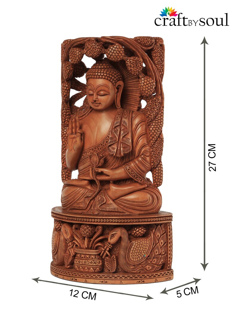 Op de afbeelding: Gedetailleerd houten Boeddha-beeld, 27 cm hoog, met ingewikkelde gravures. Het beeld zit op een decoratieve basis, 12 cm breed en 5 cm diep, met pauwen- en bloemmotieven. De tekst "craft by soul" is inbegrepen.