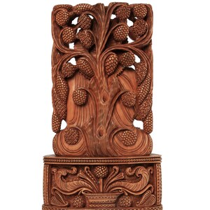 Op de afbeelding: Een gedetailleerde, bruine houten snijwerk met een boomontwerp met dennenappelachtige elementen. Het snijwerk is gemonteerd op een decoratieve basis met bloemen- en bladpatronen. Het logo "craft by soul" staat rechtsboven.