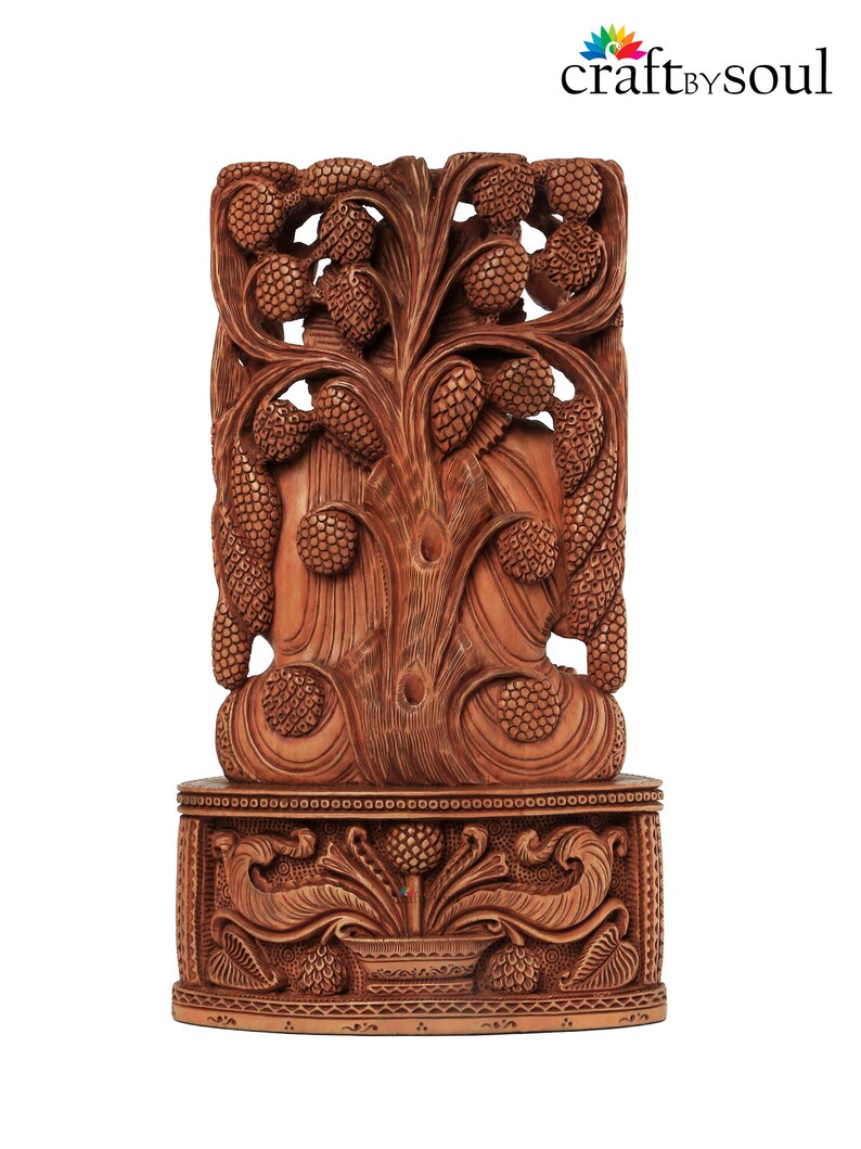 Op de afbeelding: Een gedetailleerde, bruine houten snijwerk met een boomontwerp met dennenappelachtige elementen. Het snijwerk is gemonteerd op een decoratieve basis met bloemen- en bladpatronen. Het logo "craft by soul" staat rechtsboven.