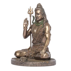Puede incluir: Estatua de color bronce de una deidad sentada, posiblemente Shiva, con pelo largo y una expresi&oacute;n serena. La figura sostiene un tridente y est&aacute; adornada con collares y una serpiente. La estatua est&aacute; sobre una base texturizada.