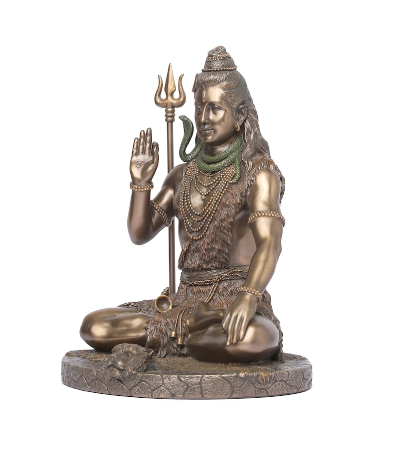 Puede incluir: Estatua de color bronce de una deidad sentada, posiblemente Shiva, con pelo largo y una expresi&oacute;n serena. La figura sostiene un tridente y est&aacute; adornada con collares y una serpiente. La estatua est&aacute; sobre una base texturizada.