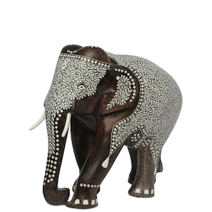 Puede incluir: Una escultura de elefante de madera hecha a mano con intrincados detalles de incrustaciones blancas. El elefante marr&oacute;n oscuro presenta colmillos y est&aacute; decorado con patrones florales y geom&eacute;tricos. La escultura es un objeto decorativo.