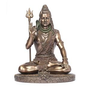 Puede incluir: Estatua de bronce de una deidad sentada, sosteniendo un tridente y adornada con una serpiente y collares en capas. La figura est&aacute; sentada en una pose meditativa sobre una base texturizada, con detalles intrincados en la ropa y las joyas.