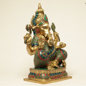 May include: A gold-colored statue of the Hindu deity Ganesha, adorned with colorful accents of green, red, and blue. The statue is intricately detailed, depicting Ganesha in a seated position with multiple arms and a large head. The base is rectangular.