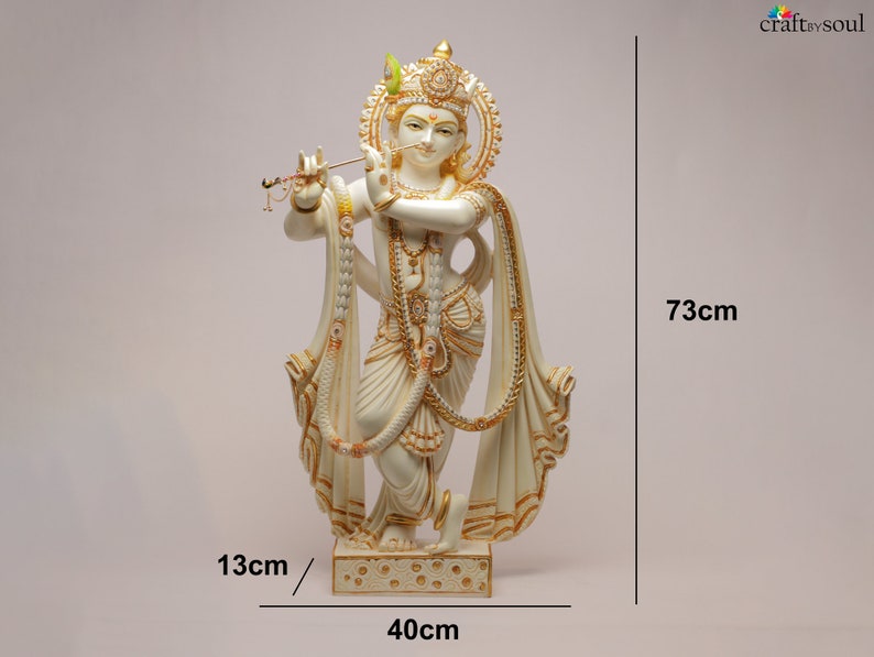 Puede incluir: Una estatua crema de Krishna, una deidad hind&uacute;, tocando la flauta. La estatua mide 73 cm de alto, 40 cm de ancho y 13 cm de profundidad. Presenta detalles dorados e intrincados, con el texto "craft by soul" visible.