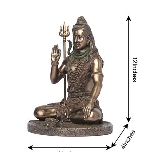 Puede incluir: Estatua de color bronce de una deidad sentada, sosteniendo un tridente y gesticulando con una mano. La estatua est&aacute; adornada con collares y una serpiente. Mide 30 cm de alto, 23 cm de ancho y 10 cm de profundidad.