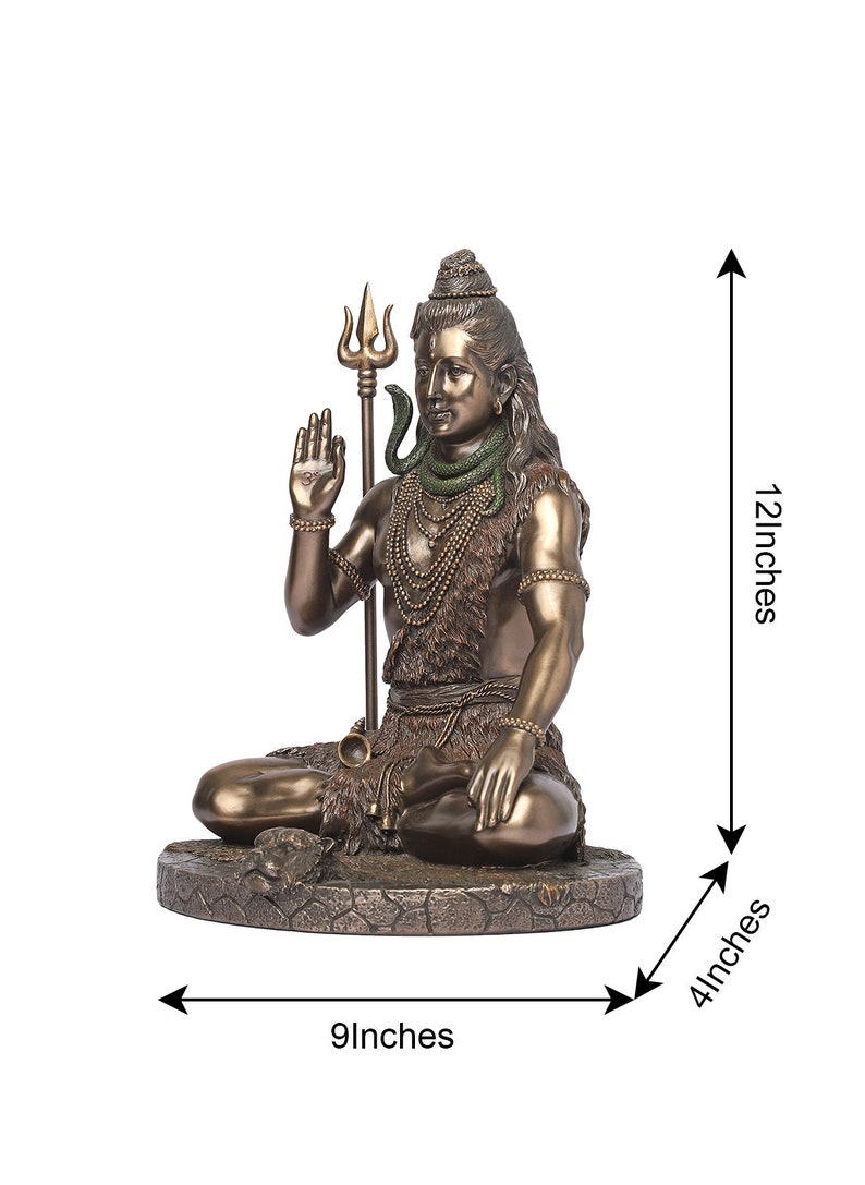 Puede incluir: Estatua de color bronce de una deidad sentada, sosteniendo un tridente y gesticulando con una mano. La estatua est&aacute; adornada con collares y una serpiente. Mide 30 cm de alto, 23 cm de ancho y 10 cm de profundidad.