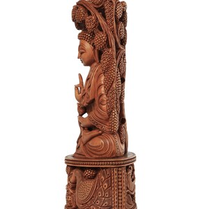 Op de afbeelding: Gedetailleerde houten sculptuur van een zittende Boeddha-figuur, gesneden uit lichtbruin hout. De sculptuur heeft ingewikkelde gravures van wijnranken en een pauw op de basis. De tekst "craft by soul" staat in de rechterbovenhoek.