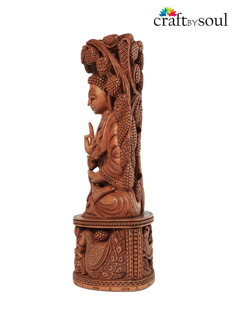 Op de afbeelding: Gedetailleerde houten sculptuur van een zittende Boeddha-figuur, gesneden uit lichtbruin hout. De sculptuur heeft ingewikkelde gravures van wijnranken en een pauw op de basis. De tekst "craft by soul" staat in de rechterbovenhoek.