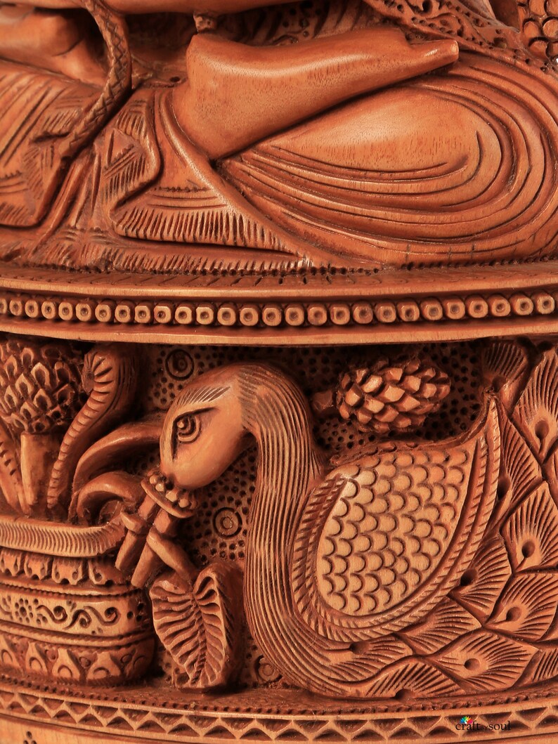 Op de afbeelding: Close-up van een gedetailleerde houten snijwerk. Het snijwerk toont een zwanenachtige vogel die een fluit bespeelt, ingewikkelde patronen en een zittende figuur. Het hout heeft een warme, natuurlijke tint, die het vakmanschap laat zien.