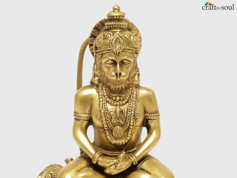 K&ouml;nnte beinhalten: Eine detaillierte Messingstatue einer sitzenden Gottheit mit affen&auml;hnlichem Gesicht, geschm&uuml;ckt mit aufwendigem Schmuck und einer Krone. Die Statue hat einen goldenen Farbton und ist vor einem schlichten Hintergrund platziert. Es ist ein religi&ouml;ses oder spirituelles Objekt.