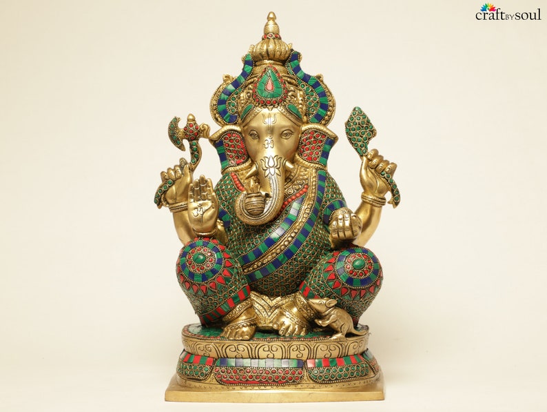 May include: A detailed brass statue of the Hindu deity Ganesha, seated with multiple arms and an elephant head. The statue is adorned with colorful mosaic-like patterns in green, blue, and red. The base is intricately designed, and the statue has a serene expression.