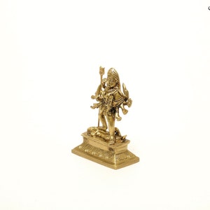 Puede incluir: Una peque&ntilde;a y detallada estatua de lat&oacute;n de una deidad de m&uacute;ltiples brazos de pie sobre una base rectangular. La estatua tiene intrincadas tallas y est&aacute; sobre un fondo blanco. La deidad est&aacute; adornada con un tocado ornamentado y sostiene varios objetos.
