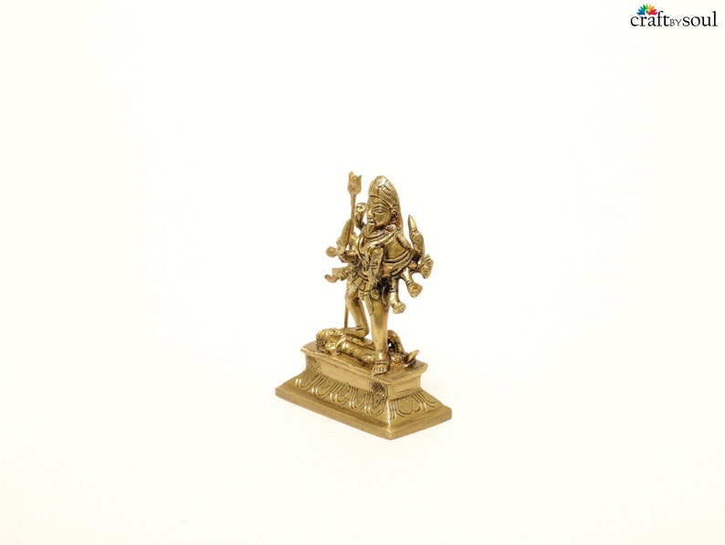 Puede incluir: Una peque&ntilde;a y detallada estatua de lat&oacute;n de una deidad de m&uacute;ltiples brazos de pie sobre una base rectangular. La estatua tiene intrincadas tallas y est&aacute; sobre un fondo blanco. La deidad est&aacute; adornada con un tocado ornamentado y sostiene varios objetos.