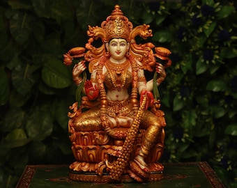 May include: A detailed, gold-colored statue of a seated deity, adorned with intricate jewelry and a crown. The figure holds lotus flowers and is seated on a lotus flower base. The statue has a serene expression and is set against a dark green background.