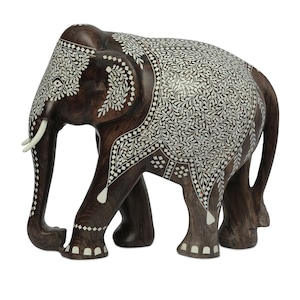 Puede incluir: Una figura de elefante de madera hecha a mano con intrincados dise&ntilde;os de incrustaciones blancas. El elefante marr&oacute;n oscuro tiene colmillos de marfil y detalles decorativos. El logotipo de Craft by Soul es visible.