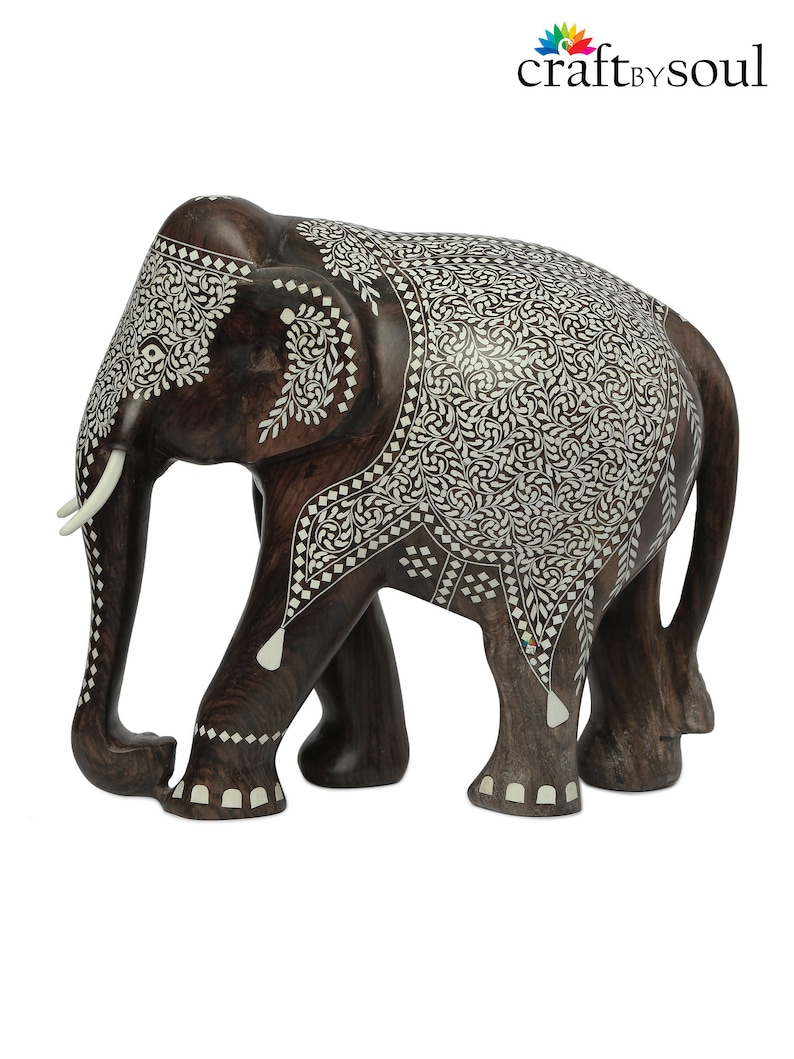 Puede incluir: Una figura de elefante de madera hecha a mano con intrincados dise&ntilde;os de incrustaciones blancas. El elefante marr&oacute;n oscuro tiene colmillos de marfil y detalles decorativos. El logotipo de Craft by Soul es visible.