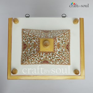 以下が含まれることがあります： 白い背景と金の縁取りが施された、装飾的な長方形の箱を真上から見た図。箱には、赤、緑、金色の詳細な花柄のデザインが施されています。角には金のアクセントがあり、上部には中央に金のノブがあります。