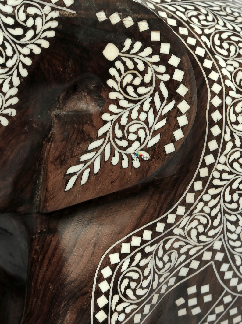 Puede incluir: Primer plano de un objeto de madera marr&oacute;n oscuro con intrincados dise&ntilde;os de incrustaciones blancas. La incrustaci&oacute;n presenta patrones florales y geom&eacute;tricos, creando una superficie decorativa y detallada. La veta de la madera es visible.