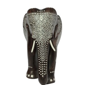 Puede incluir: Una figura de elefante de madera marr&oacute;n oscuro con intrincados patrones de incrustaciones blancas. El elefante tiene colmillos de color marfil y tallas detalladas en la cabeza y el cuerpo. Es un objeto decorativo.