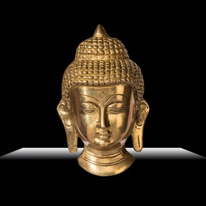 Puede incluir: Una escultura de cabeza de Buda dorada con los ojos cerrados y cabello detallado. La escultura tiene una expresi&oacute;n serena y est&aacute; sobre un fondo negro. La cabeza est&aacute; hecha de un material met&aacute;lico brillante.