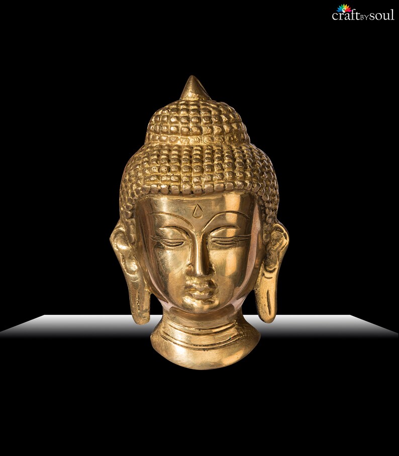 Puede incluir: Una escultura de cabeza de Buda dorada con los ojos cerrados y cabello detallado. La escultura tiene una expresi&oacute;n serena y est&aacute; sobre un fondo negro. La cabeza est&aacute; hecha de un material met&aacute;lico brillante.