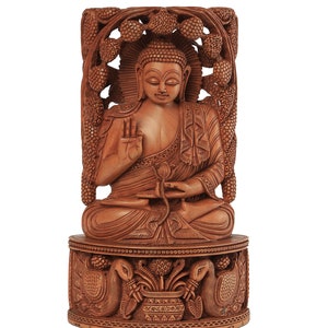 Op de afbeelding: Een gedetailleerd houten Boeddha-beeld in een zittende meditatiehouding. Het beeld is gesneden uit lichtbruin hout en heeft ingewikkelde details, waaronder een halo, sierlijke gravures en een decoratieve basis met pauwen. Het Craft by Soul-logo staat rechtsboven.