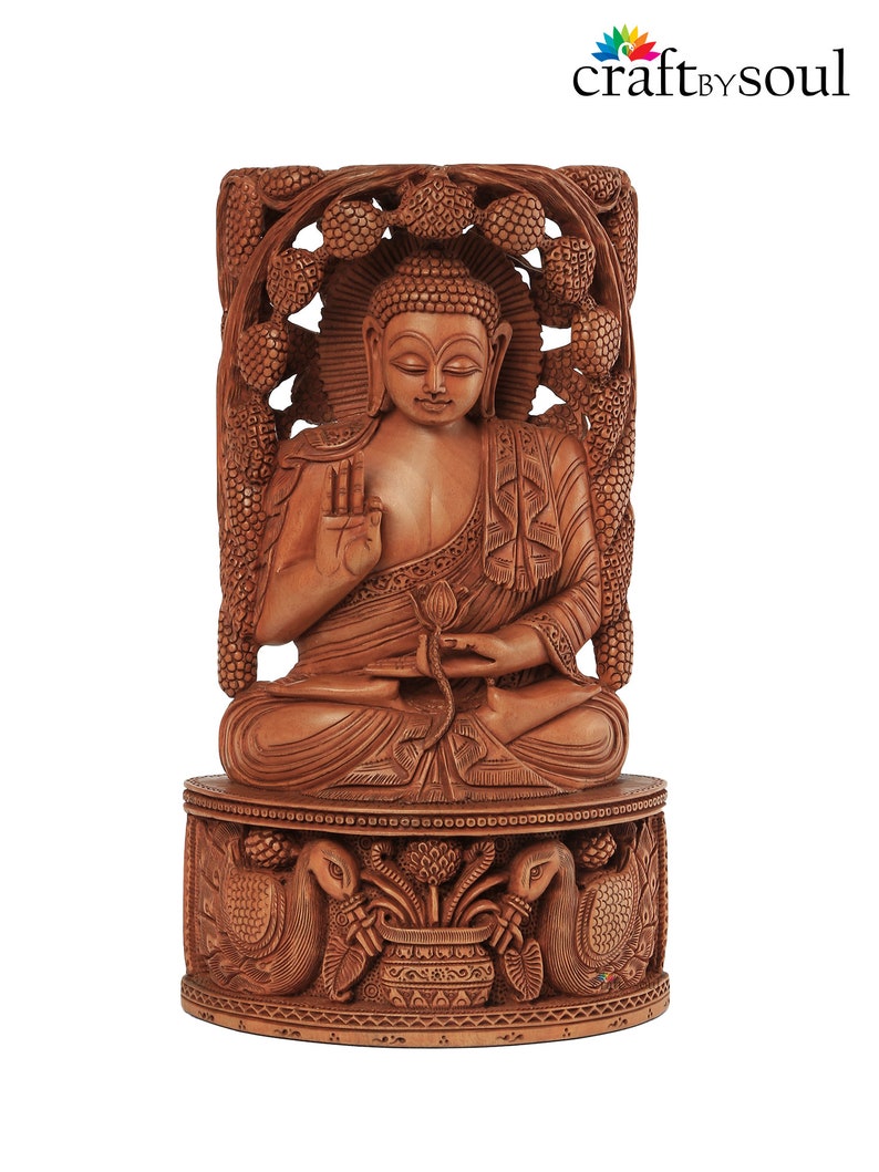 Op de afbeelding: Een gedetailleerd houten Boeddha-beeld in een zittende meditatiehouding. Het beeld is gesneden uit lichtbruin hout en heeft ingewikkelde details, waaronder een halo, sierlijke gravures en een decoratieve basis met pauwen. Het Craft by Soul-logo staat rechtsboven.
