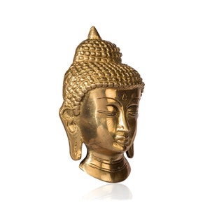 Puede incluir: Una escultura de cabeza de Buda dorada con los ojos cerrados y rasgos faciales detallados. La escultura tiene un dise&ntilde;o de cabello texturizado y una parte superior puntiaguda. Sobre un fondo blanco.