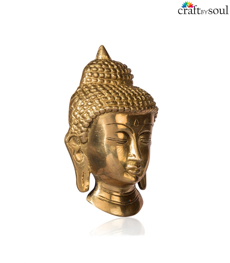 Puede incluir: Una escultura de cabeza de Buda dorada con los ojos cerrados y rasgos faciales detallados. La escultura tiene un dise&ntilde;o de cabello texturizado y una parte superior puntiaguda. Sobre un fondo blanco.