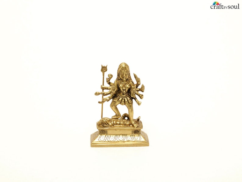Puede incluir: Una peque&ntilde;a y detallada estatua de lat&oacute;n de una deidad de m&uacute;ltiples brazos, de pie sobre una base rectangular. La figura est&aacute; adornada con intrincados detalles y sostiene varios objetos. La estatua est&aacute; sobre un fondo blanco liso.